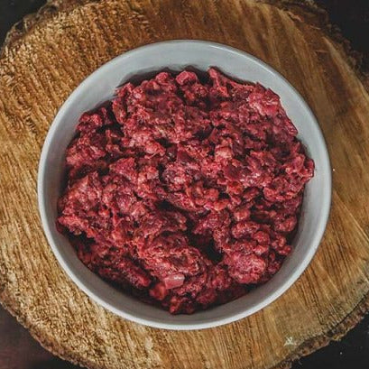 Raw ground beef in a white bowl on a wooden surface