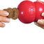 Red KONG dog toy with a bone-shaped treat held by two hands on a white background