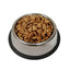 A stainless steel pet food bowl filled with dry kibble, set on a black rubber mat against a plain white background. It contains dr jaynes beef dry dog food kibble.