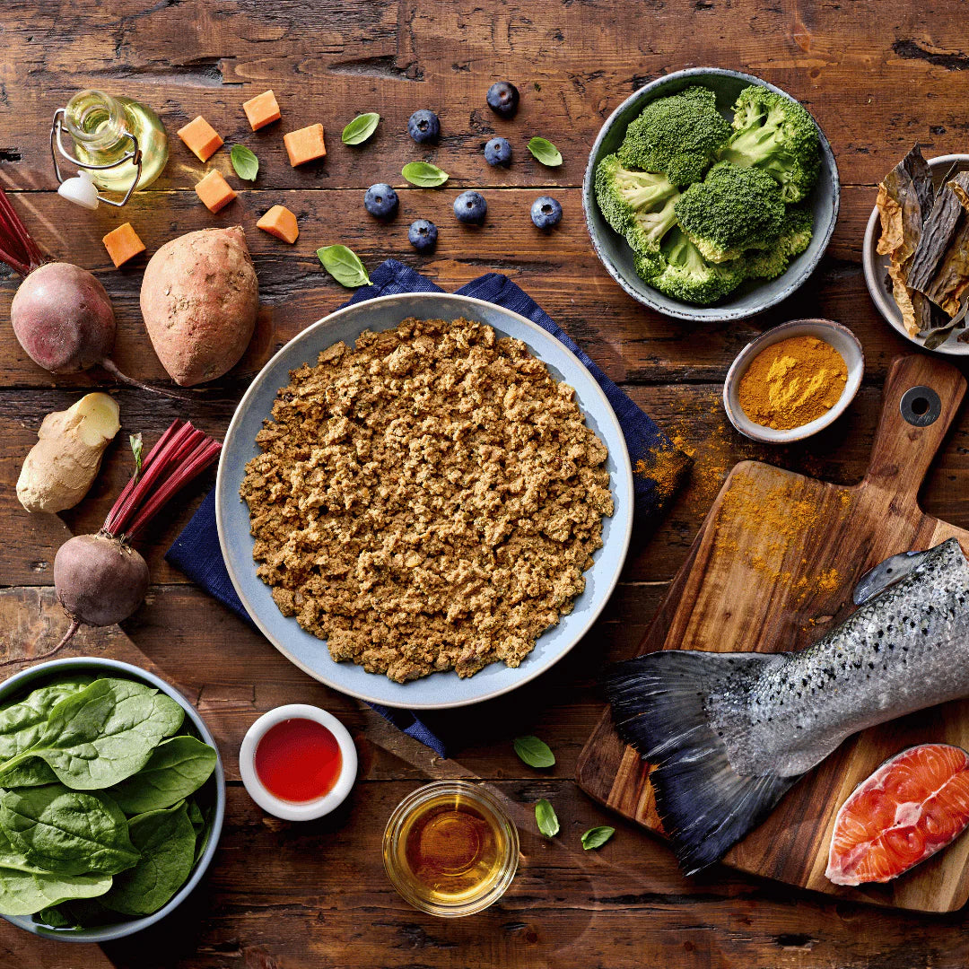 Assorted healthy foods including a bowl of ground meat, vegetables, and fish on a wooden table.