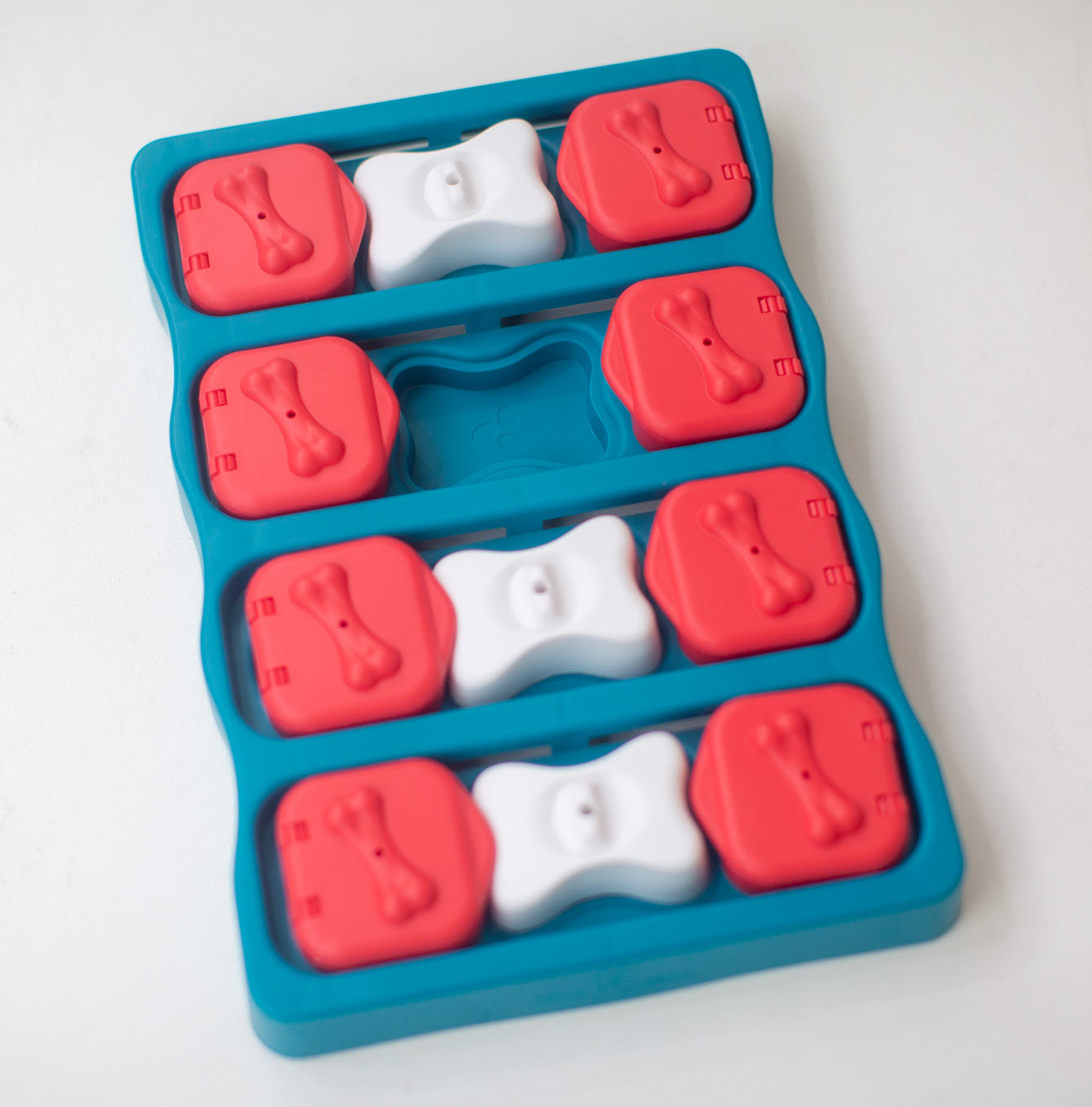 Treat puzzle dog toy with red and white bone-shaped cavities on a white background