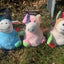 Three colorful plush dog toys on grass with packaging in the background