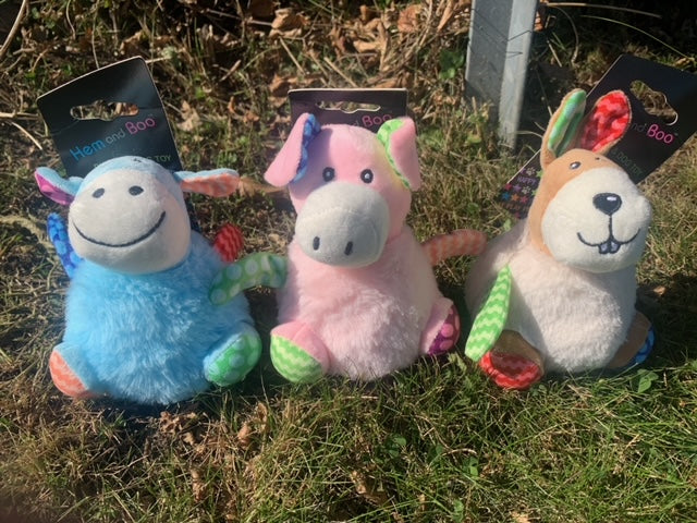 Three colorful plush dog toys on grass with packaging in the background