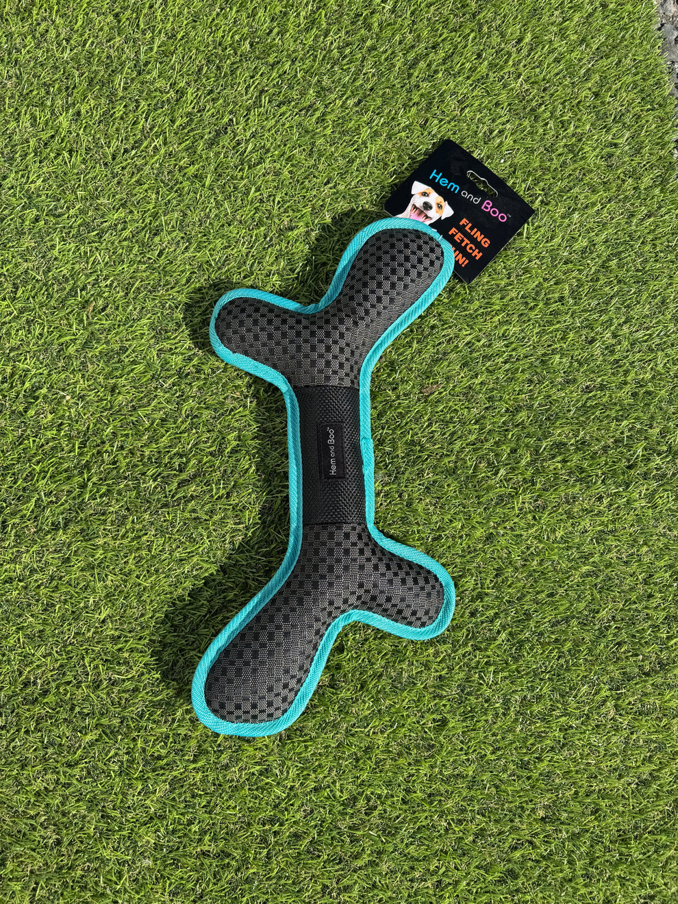 Black and teal dog toy on grass with a brand label.