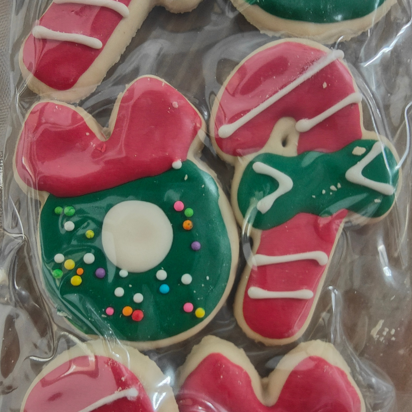 Decorative dog cookies shaped like a candy cane and a wreath with green, red, and white icing on a clear background.
