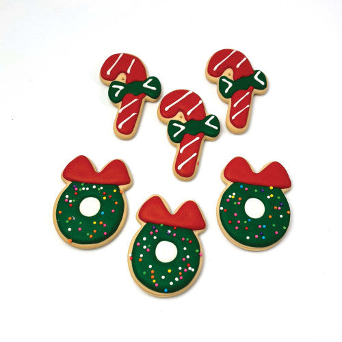Decorative dog biscuits or cookies shaped like candy canes, wreaths, and bows on a white background