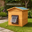 A wooden outdoor cat kennel with a slanted roof and a flap door, shown on a grassy garden lawn. A dark green banner at the top reads 'WARM & SECURE'. It is a weatherproof cat kennel available in Ireland and UK at PetConnection